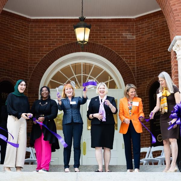 A group of people hold scissors in the air after a ribbon cutting for a renovated building